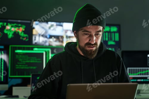 Preview: Male hacker with beard working near computer monitors with data on screens on black