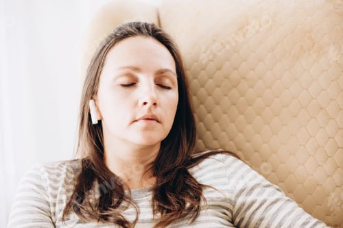 Preview: Brunette girl resting in cozy armchair with wireless headphones and listening to music or audiobook.