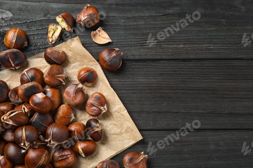 Preview: Tasty roasted edible chestnuts on black wooden table, flat lay. Space for text