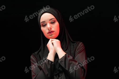 Preview: Portrait of beautiful serious young muslim woman wearing black hijab with closed eyes as praying