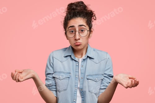 Preview: Photo of pretty mixed race female with puzzled expression, shrugs shoulders, has uncertain look, wea
