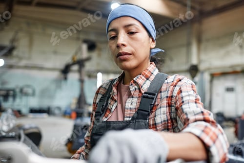 Preview: Young Hispanic workwoman or repairperson in coveralls, blue headband and gloves