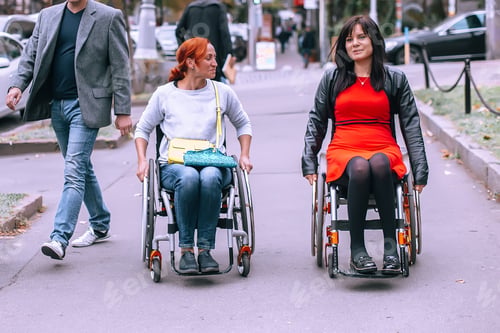 Preview: Two girls on wheelchairs in the city near the walking men of the townspeople.