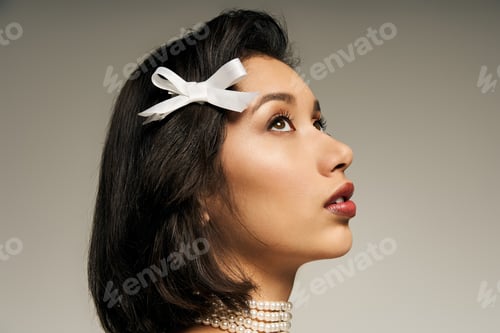 Preview: Young bride elegantly posed, with a ribbon hair accessory and pearl necklace, radiating beauty