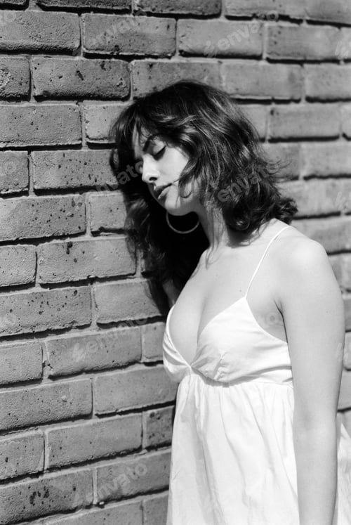 Preview: Analog portrait of young woman leaning on brick wall with eyes closed.