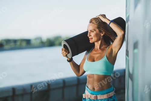 Preview: Woman Holding Rolled Up Exercise Mat After Training Near The River