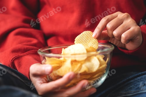 Preview: Closeup image of a woman picking and eating potato chips at home