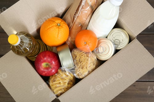 Preview: Cardboard box with donation food on wooden table, top view