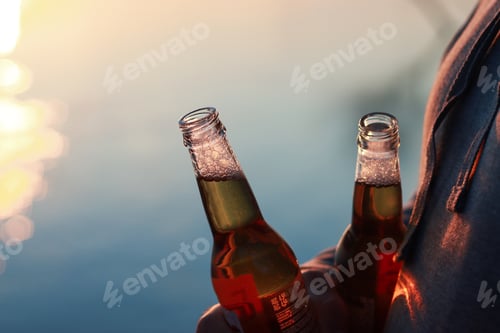 Preview: The man is standing by the river, holding a beers in his hand.