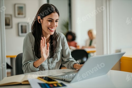 Preview: Smiling businesswoman waving during a video call in the office