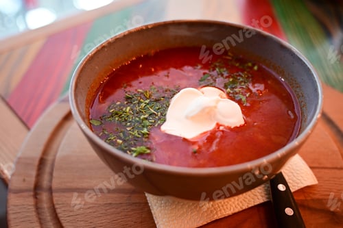 Preview: Russian traditional dish borscht with herbs and sour cream in a semicircular plate on a wooden board