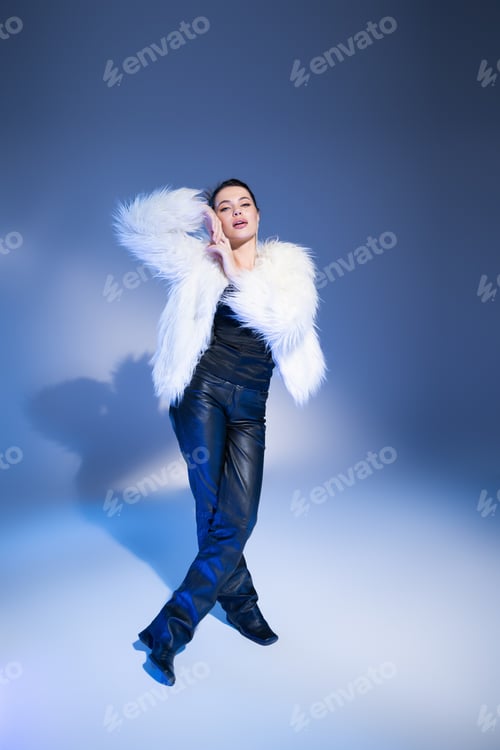 Preview: Full length of trendy brunette model in faux fur jacket posing on blue background