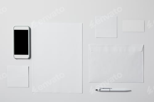 Preview: top view of smartphone with various blank papers and pen on white tabletop for mockup