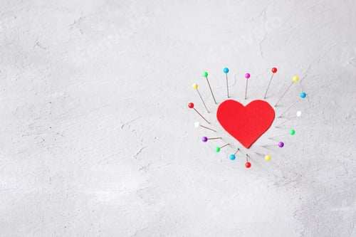 Preview: Red paper heart and multicolored sewing pins on gray cement background. Hard love, loneliness