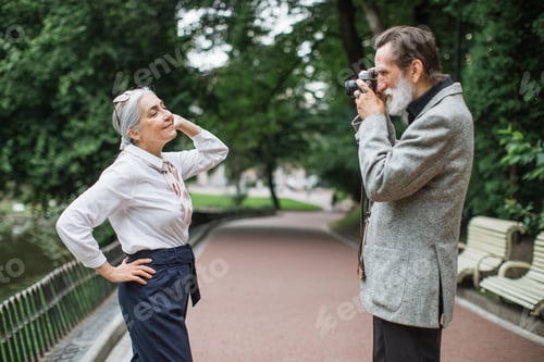 Preview: Smiling aged man taking photo of lovely wife on retro camera
