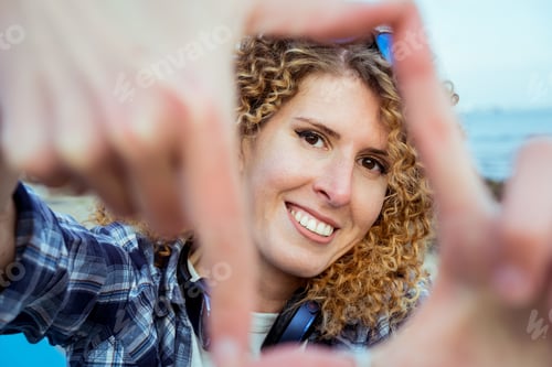 Preview: Portrait of smiling curly hair woman looking through a frame made of fingers. capture the moment