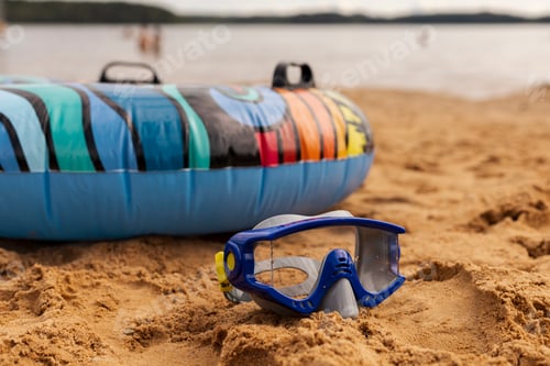Preview: Bright inner tube sits on the warm sand next to a snorkel mask, with calm waters