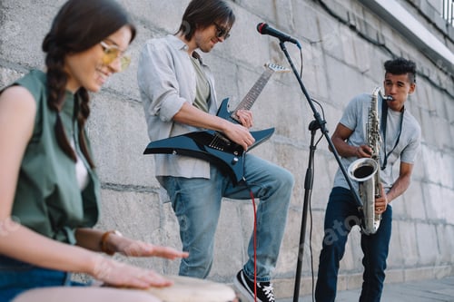 Preview: Multiracial young musical band with guitar, drum and saxophone performing on street