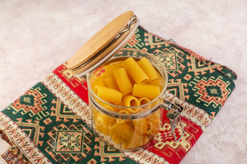Preview: a front view raw italian pasta inside little glass kettle on the colorful carpet and light