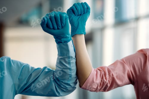Preview: Close-up of coworkers elbow bumping while greeting in a hallway.