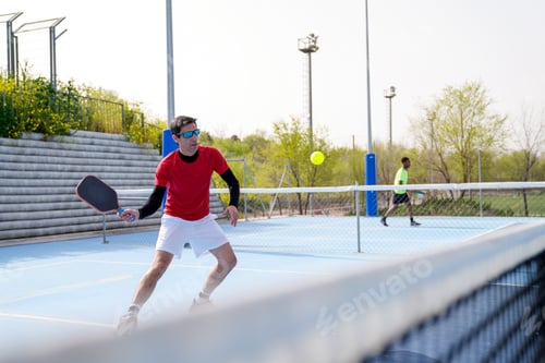 Preview: Focused player prepares for a forehand shot during an outdoor pickleball match.