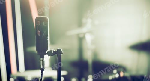 Preview: Microphone in recording Studio or concert hall close-up, with drum set on background out of focus.