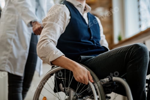 Preview: Unrecognizable nurse pushing wheelchair of male patient.