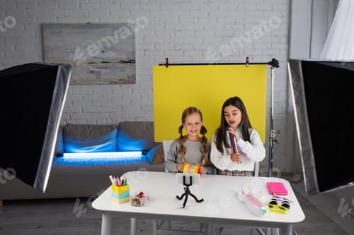 Preview: blogger showing copybook near friend with spiral toy while sitting on yellow background near