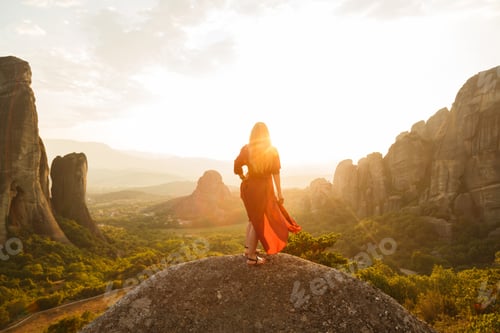 Preview: Young woman in red dress looking at majestic sunset in Meteora valley, Greece