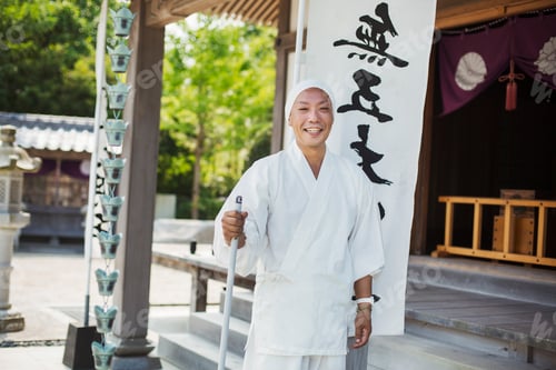 Preview: Buddhist monk wearing white robe and cap standing outside a temple, smiling at camera.