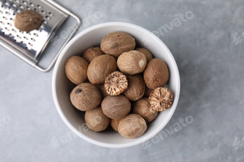 Preview: Nutmegs in bowl and metal grater on light grey table, flat lay