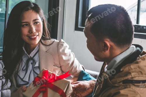Vista previa: Young man is giving a present to his lovely girlfriend while they are sitting on couch at home