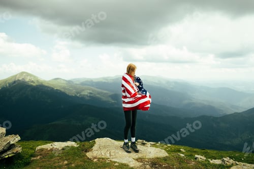 Preview: Female is waving American flag on top of mountain at sky background