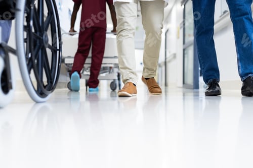 Preview: Low section of diverse male doctors and wheelchair in busy hospital corridor, copy space