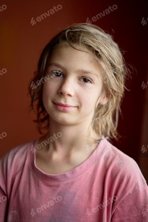 Preview: Portrait of a smiling young boy with curly hair in a pink t-shirt against a warm-toned background.