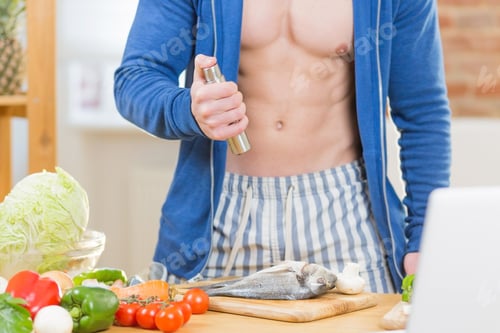 Preview: Portrait of young handsome athletic man learning to cook fish with fresh vegetables online with