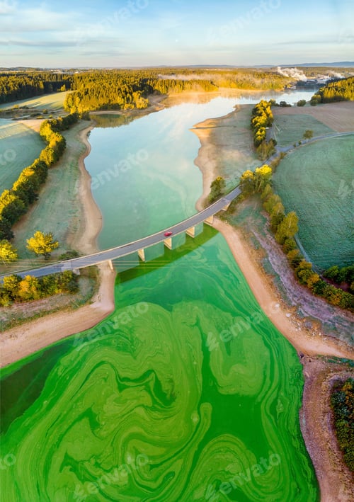 Preview: Aerial view of a bridge above the green lake surrounded by forest and agricultural fields at sunset