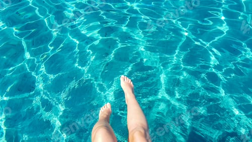 Preview: Personal perspective image of Woman's legs dangling over transparent turquoise sea water.
