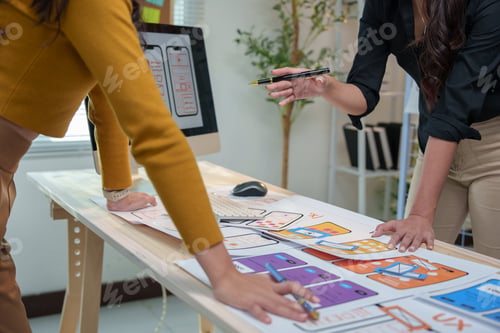 Preview: Two female ux designers are collaborating on wireframes for a mobile app, meticulously reviewing and