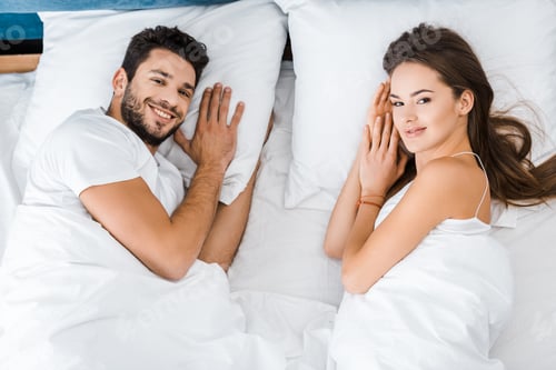 Preview: top view of young couple lying in bed and looking at camera
