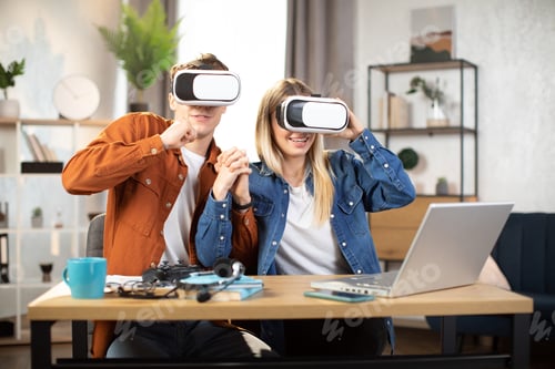 Preview: Caucasian couple in VR glasses sitting at the table with laptop