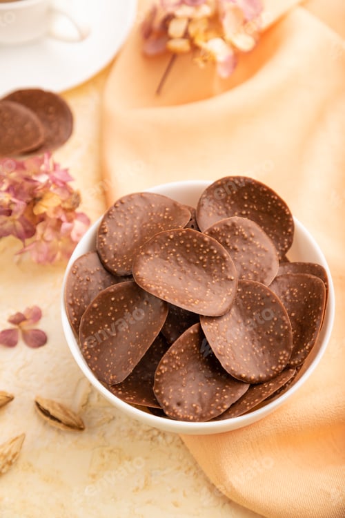Preview: Chocolate chips with cup of coffee and caramel on a beige concrete background and orange textile