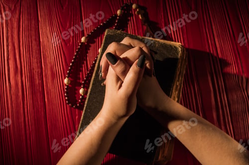 Preview: Top view folded young demale hands onholy bible cover with rosary.