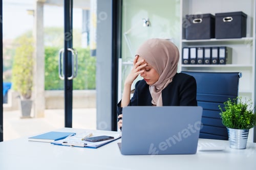 Preview: Muslim businesswoman, donning a hijab, diligently works at her desk.