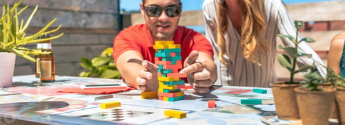 Preview: Concentrated young man pushing jenga game piece next to female friend in rooftop party