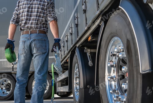 Preview: Transportation Worker Prepares to Secure Cargo on a Large Truck at a Loading Dock in Bright Sunlight