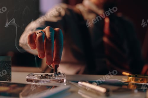 Preview: Close-up of hand of young man stubbing butt of cigarette in ashtray