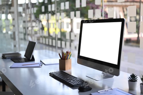 Preview: Side view of computer with blank screen and tablet on modern workstation.