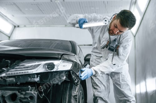 Preview: Front view. Garage worker is holding lighting and checking surface of the car