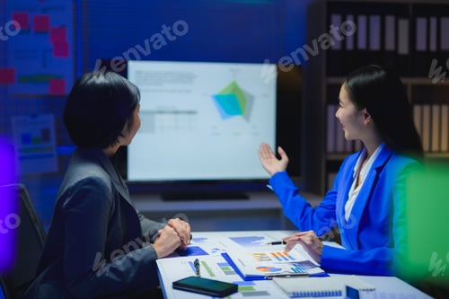 Preview: Businesswomen working late at night analyzing financial charts on a monitor